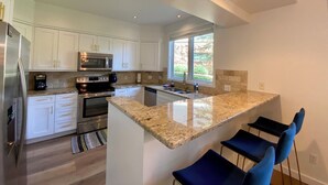 A modern kitchen with white cabinets, stainless steel appliances, a granite countertop, and a large window providing natural light. -  Modern Mountain Retreat - Ski-in-out - Heated Pool and Hot Tub (Steamboat Springs)