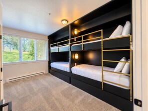 A room with bunk beds, a window with blinds, and a radiator.