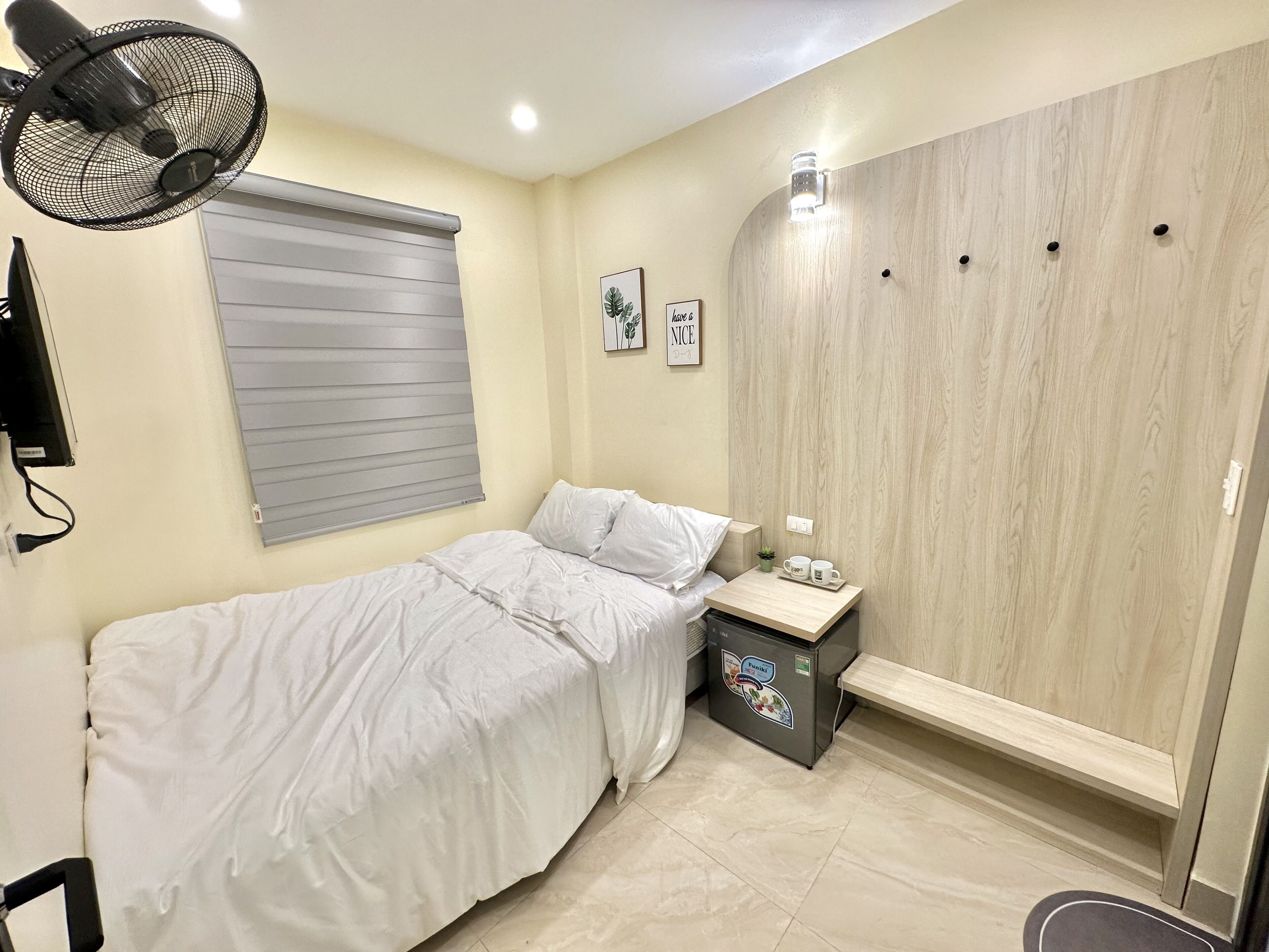 A bedroom with a bed, a bedside table with a lamp, a small plant, and a wall-mounted wardrobe.