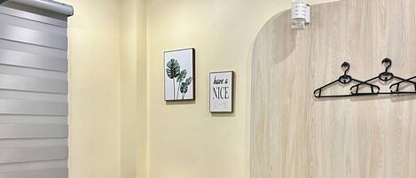 A neatly arranged hotel room with a bed, a bedside table with a lamp, a small stool, and a wall-mounted coat rack.