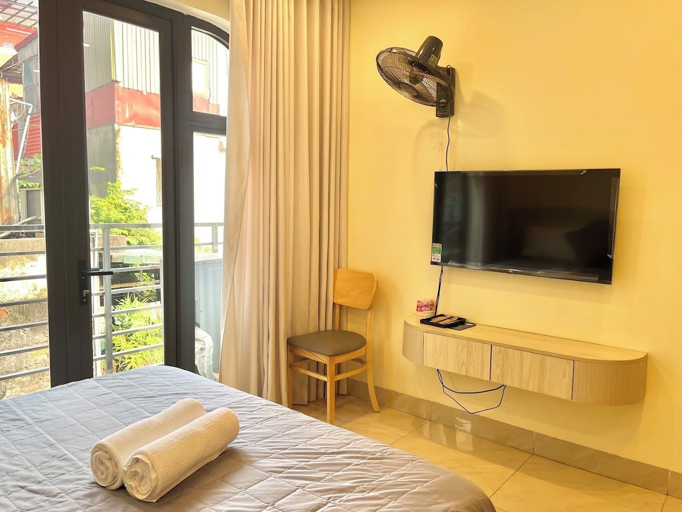 A hotel room with a bed, a TV mounted on the wall, a chair, and a window with curtains.