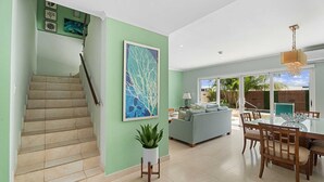 Un vaste espace de vie comprenant un escalier, un grand tableau, une table à manger avec des chaises et une vue sur l’extérieur.