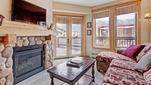 A cozy living room with a stone fireplace, a flat-screen TV, a sofa, and a balcony with a view of the mountains. - A Skiers Paradise, Short Walk to Lift. TX202 (Copper Mountain)