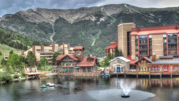 A lakeside hotel with multiple buildings, a dock, and a mountain backdrop. - A Skiers Paradise, Short Walk to Lift. TX202 (Copper Mountain)