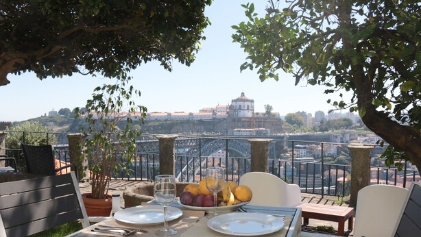 Área de refeições ao ar livre com mesa posta para dois, com vista para um horizonte urbano e uma estrutura em cúpula imponente.