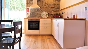 Uma cozinha com parede de pedra, piso de madeira, armários brancos, uma torradeira vermelha e um forno embutido.