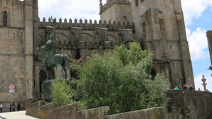 Um edifício histórico com uma grande torre do relógio, uma estátua e uma carrinha branca estacionada nas proximidades.