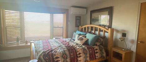 Ein Schlafzimmer mit einem hölzernen Bett, einem Nachttisch, einem Deckenventilator und einem Fenster mit Jalousien.