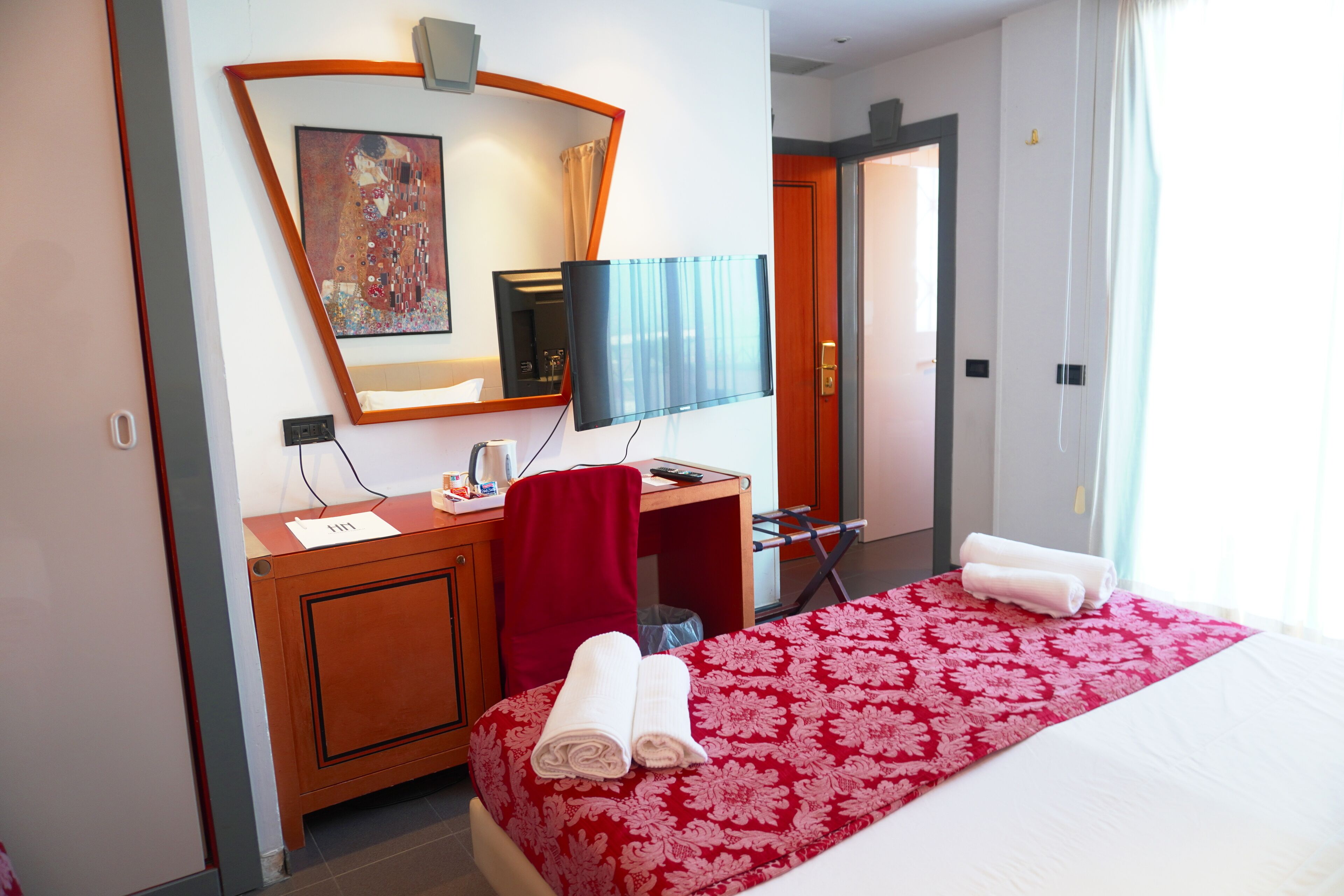 Habitación de hotel con cama, escritorio, silla, televisión y puerta.