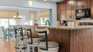 Une cuisine moderne avec des meubles en bois, un micro-ondes noir et un coin bar avec des tabourets.