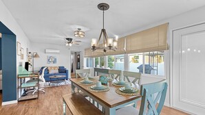 Un vaste espace de vie comprenant une table à manger en bois, des chaises bleues et un ventilateur de plafond.