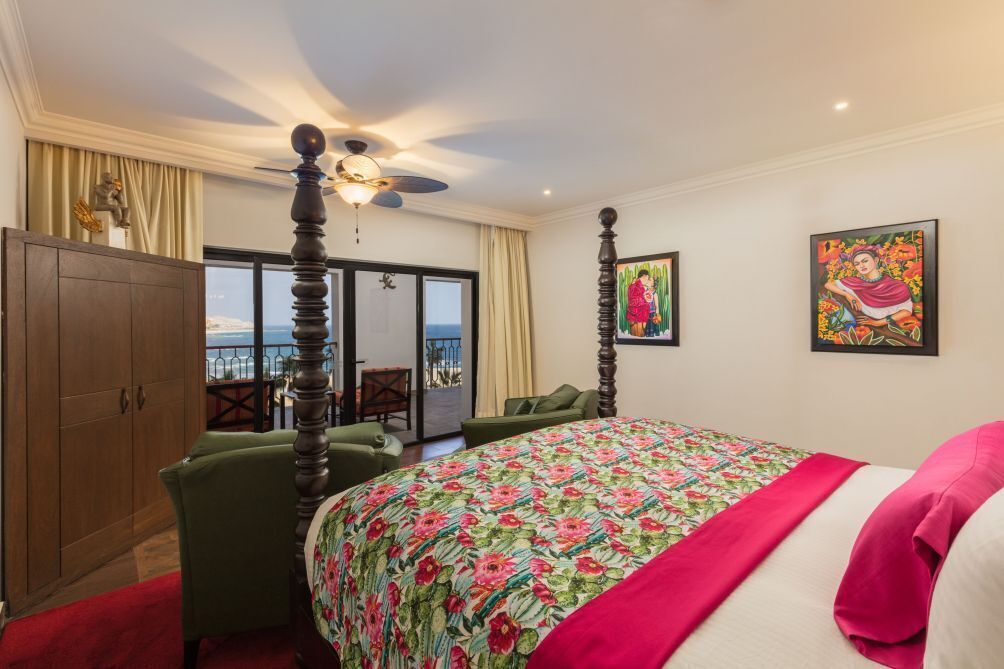 A bedroom with a large bed, a wardrobe, a ceiling fan, and a view of the sea through a sliding door.