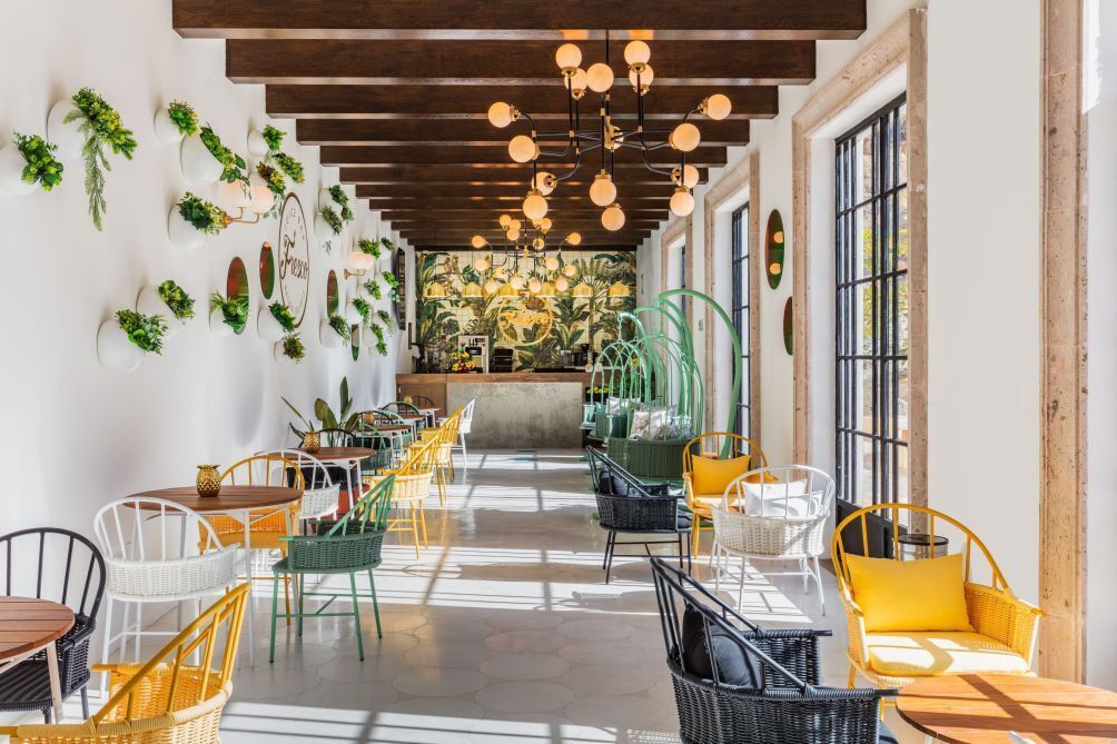 A spacious indoor area with multiple seating arrangements, including wicker chairs and tables, and a central area with a counter and plants.