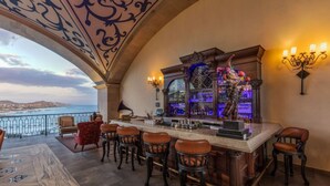 A bar area with a view of the sea, bar stools, and a decorative bar counter.