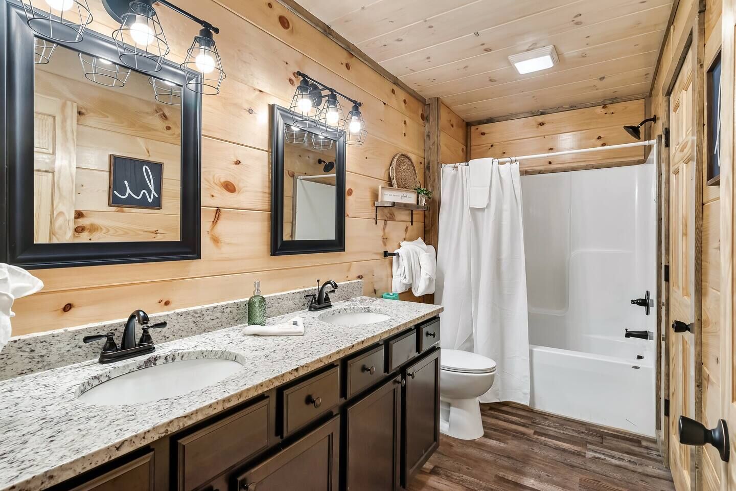 A wooden cabin bathroom with two sinks, a toilet, and a shower.