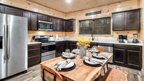 A modern kitchen with dark wooden cabinets, stainless steel appliances, a granite countertop, and a dining area set for four. - Smokies Cabin: Dog-Friendly, Hot Tub & Arcade Game (Sevierville)
