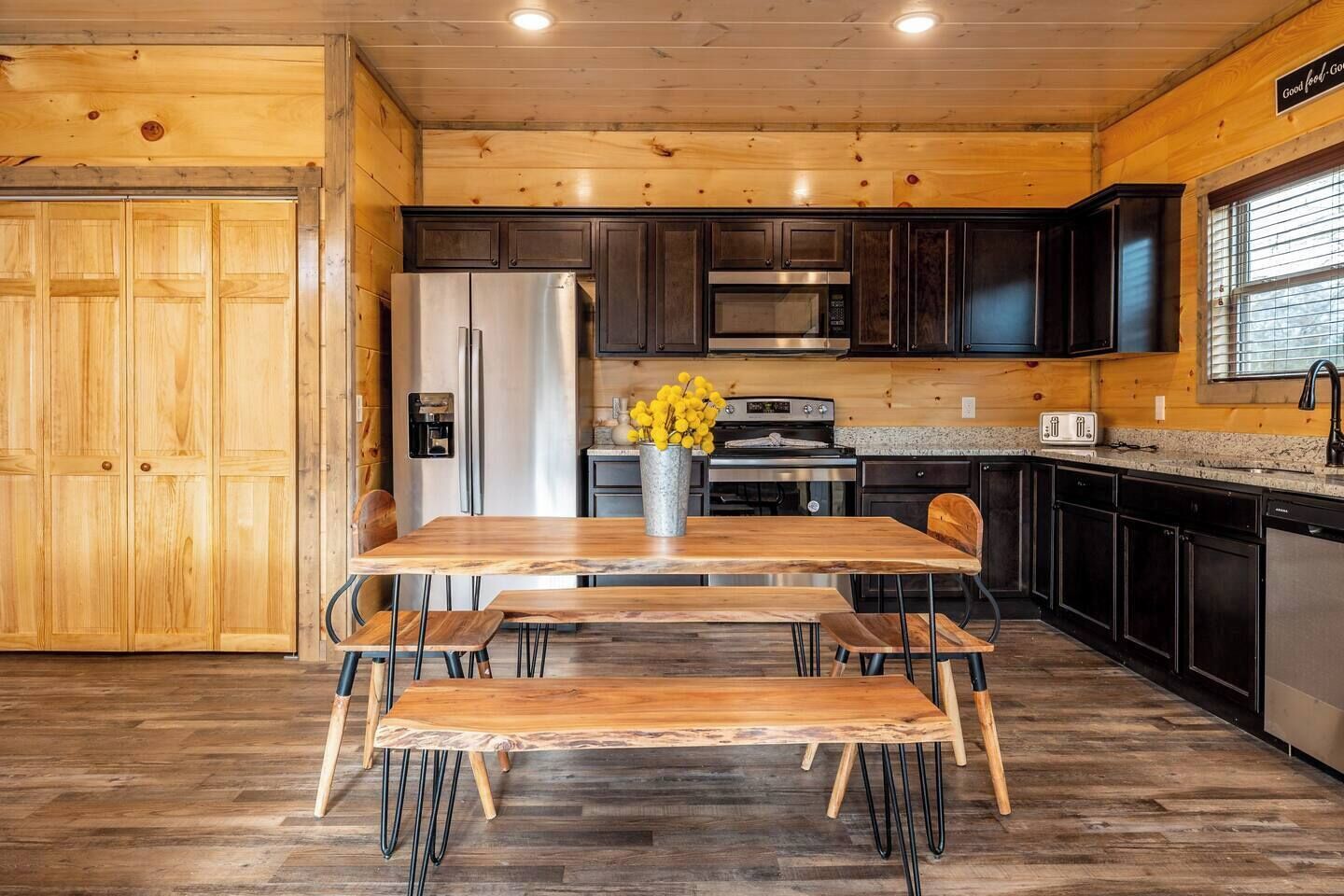 A wooden interior with a kitchen area featuring dark cabinets, stainless steel appliances, and a wooden dining table with benches.