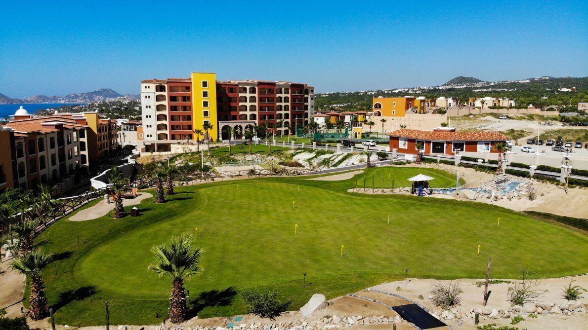 A hotel with multiple buildings, a well-maintained lawn, and a view of the sea.