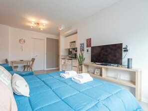 A bedroom with a large bed, a TV, a desk, and a kitchenette.