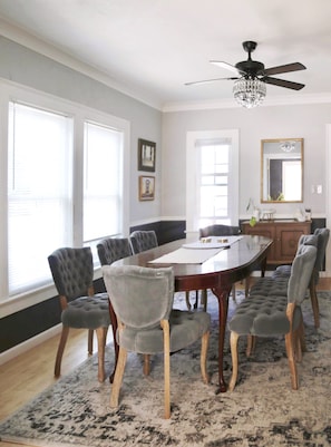 A dining room with a large table, six chairs, and a chandelier.