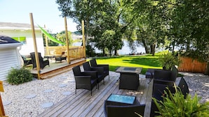 A wooden deck with outdoor furniture, a grassy lawn, and a view of a body of water. - Riverfront Getaway (Two Rivers)