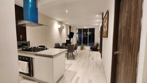 Una cocina moderna con una isla central, un comedor con mesa y sillas, y vista al salón.