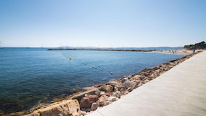 A coastal walkway with a rocky shoreline, clear blue water, and distant sailboats. - Nice studio with terrace port de hyeres (Hyères)