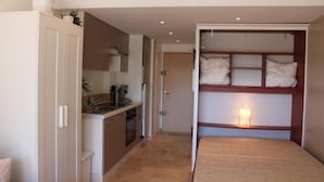 A compact room with a kitchenette, a bed with storage, and a small bedside table with a lamp. - Nice studio with terrace port de hyeres (Hyères)