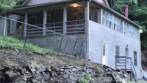 Ett tvåvåningshus med en balkong, en skorsten och en mur av sten som används som stödmur.