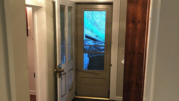 En hall med en stängd dörr, ett träkarm och ett klinkergolv.