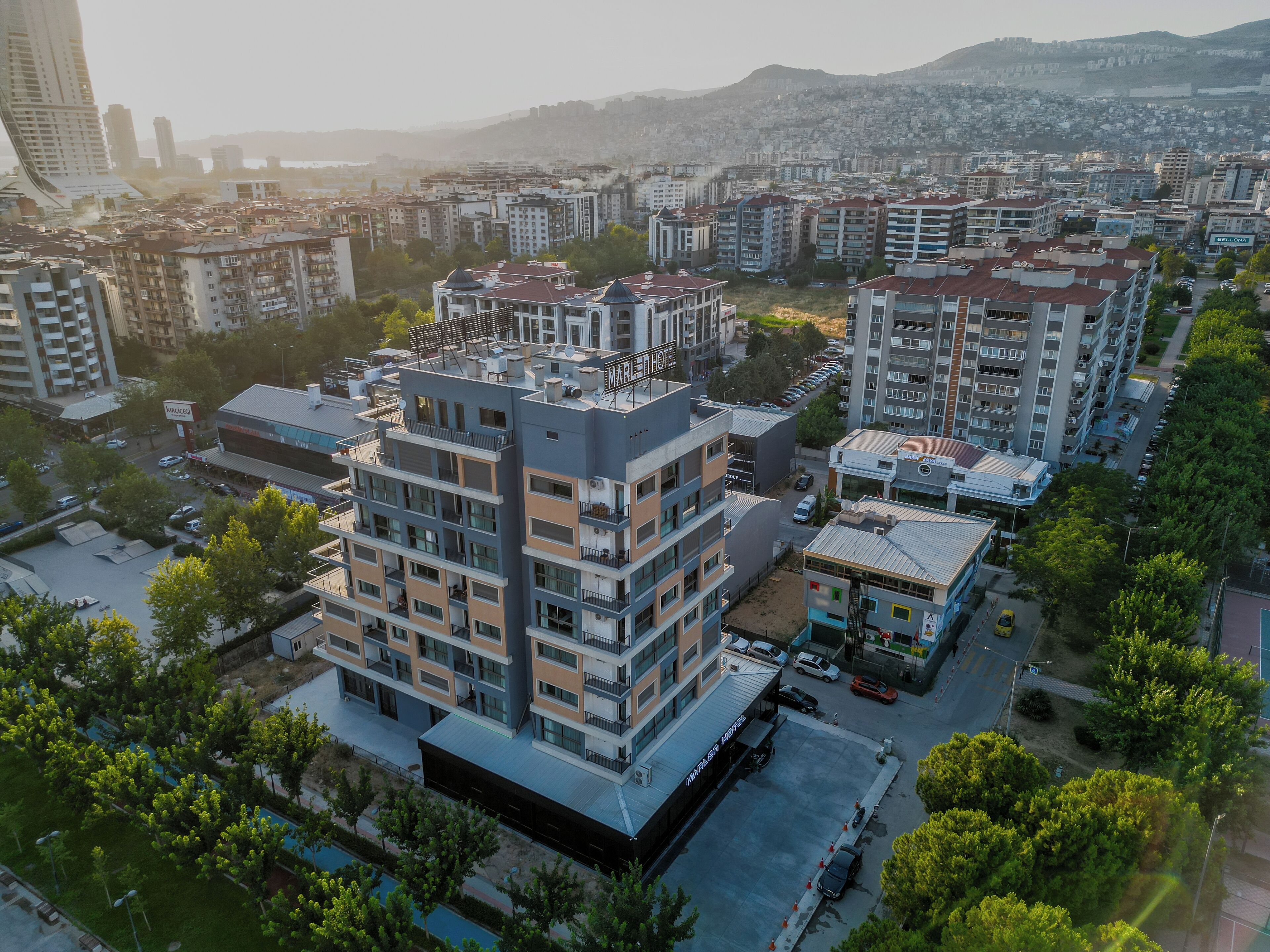 A multi-story hotel with a modern design, featuring balconies and a parking area.
