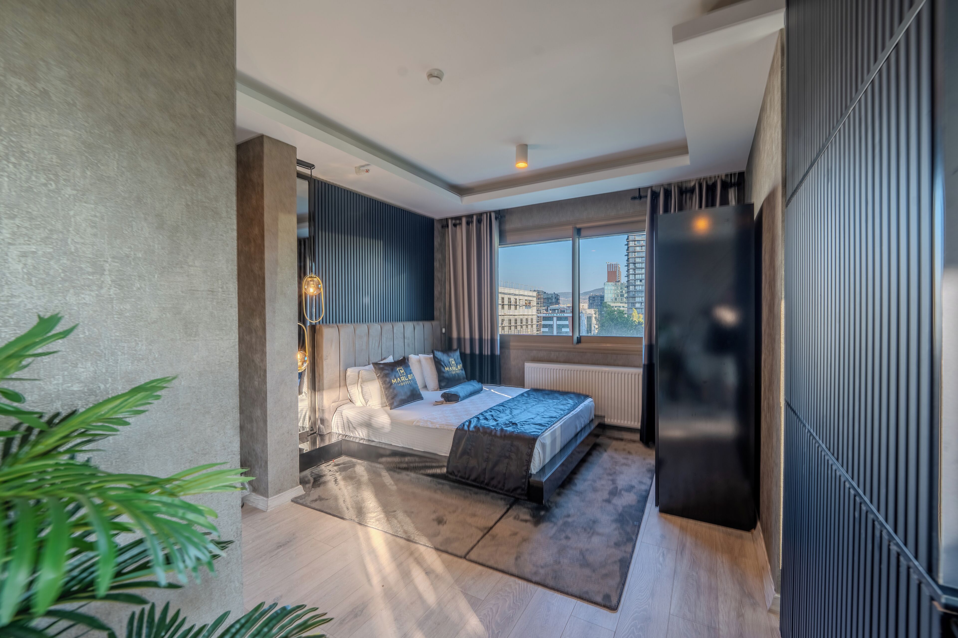 Quarto de hotel moderno com uma cama grande, vista da cidade e uma janela ampla.