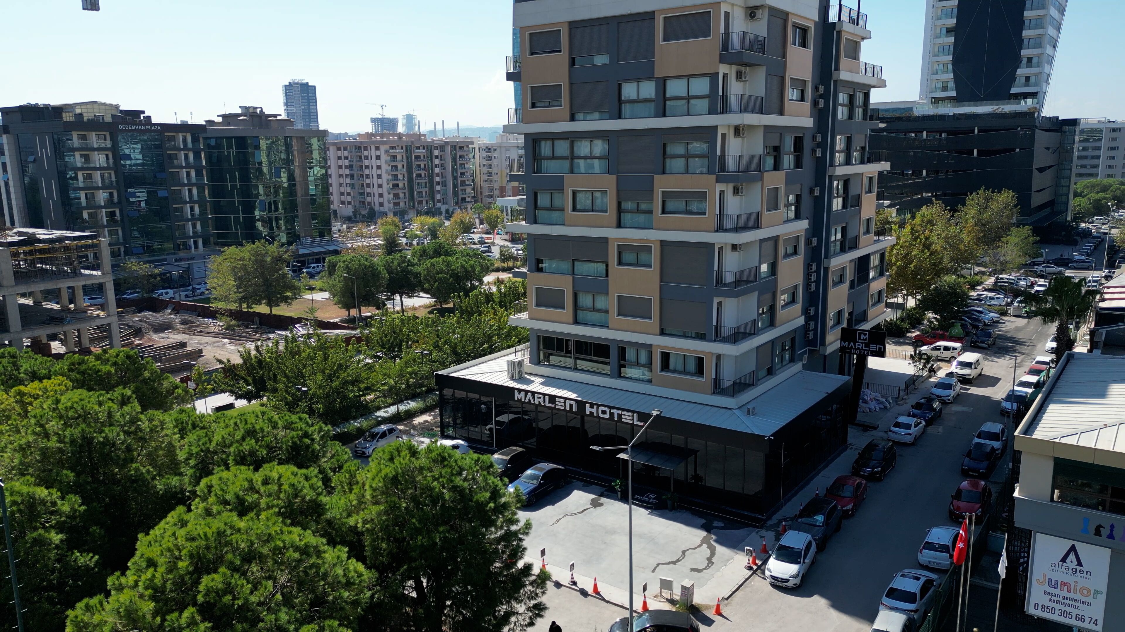 A multi-story hotel with a modern design, featuring balconies on each floor and a parking area in front.