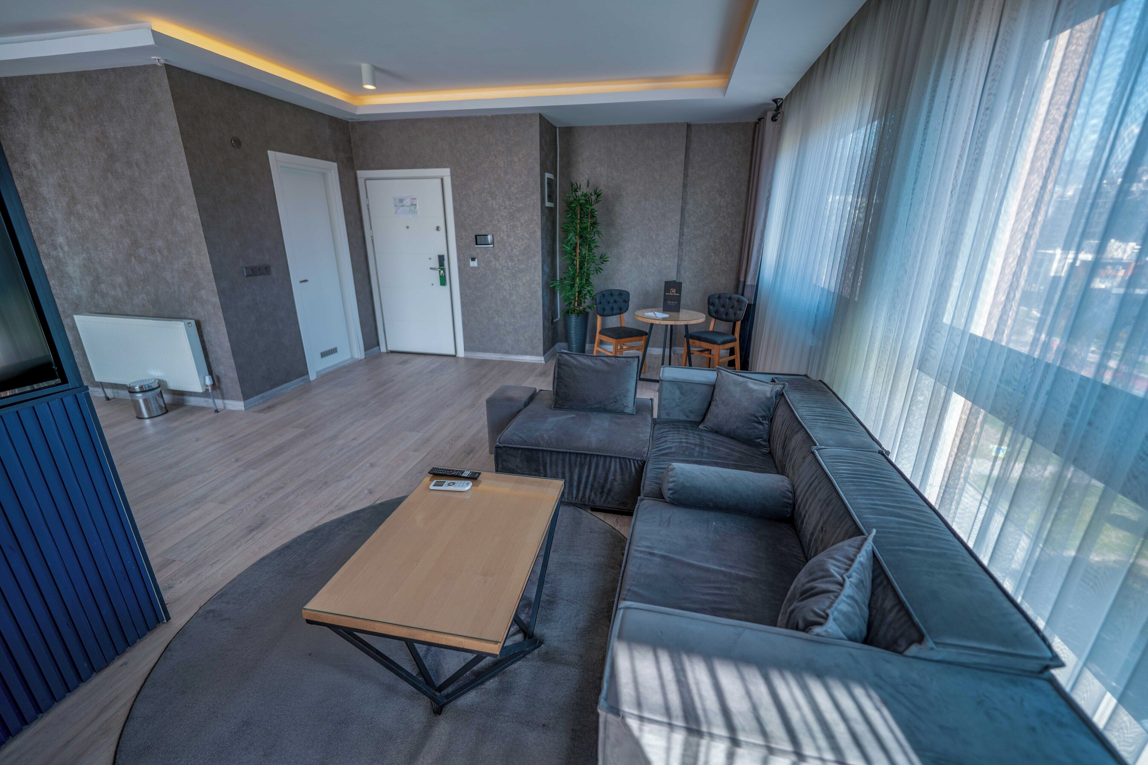 A modern living room with a sofa, a coffee table, and a small table with chairs. There is a door and a potted plant in the background.