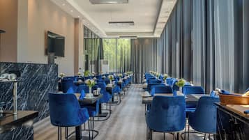 A modern dining area with blue chairs, marble countertops, and a long table with flowers.