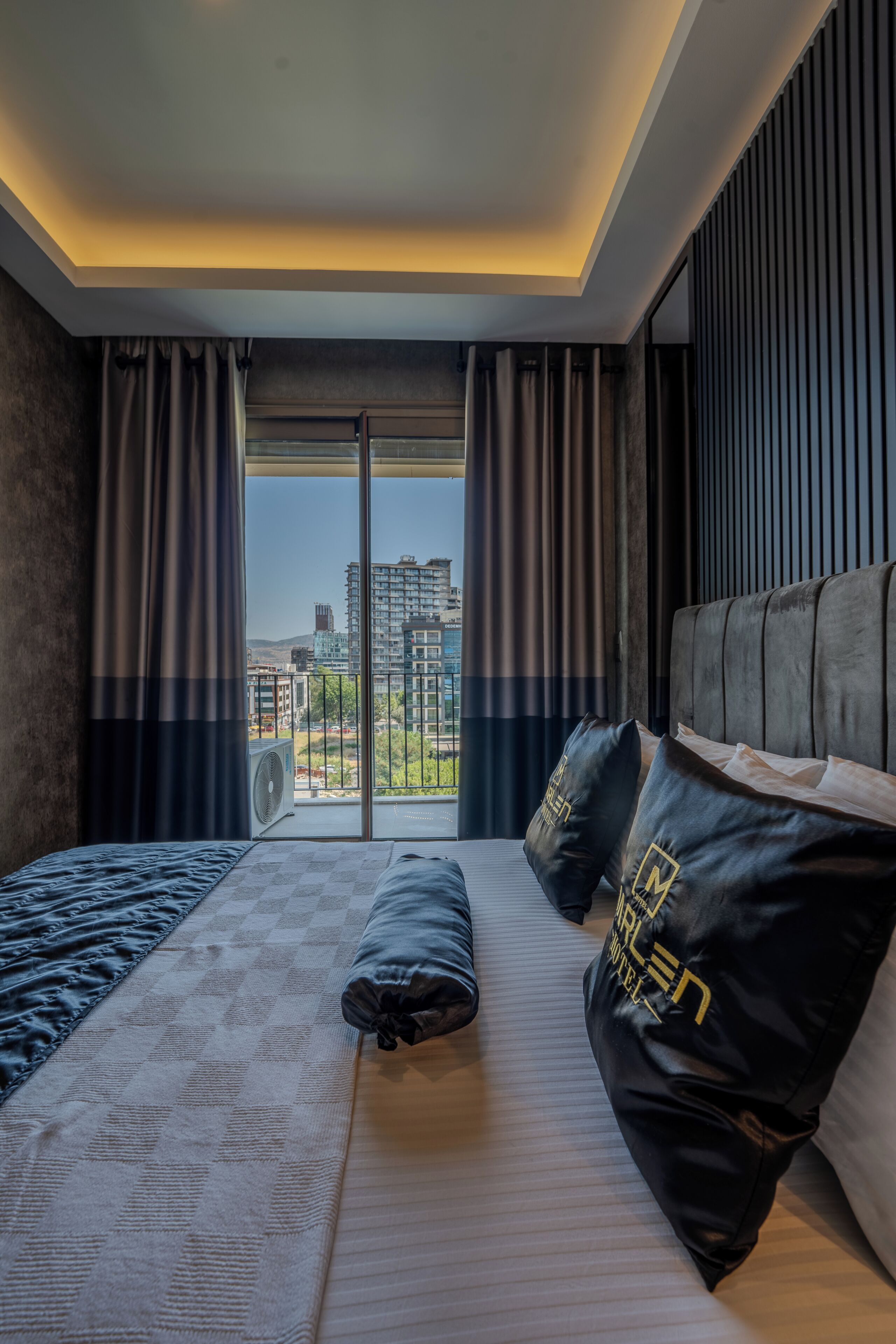 A modern hotel room with a large bed, a view of the city through floor-to-ceiling windows, and a cityscape visible outside.