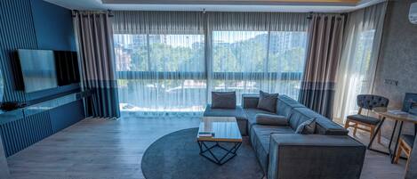 A modern living room with a sectional sofa, a coffee table, and a flat-screen TV mounted on the wall.