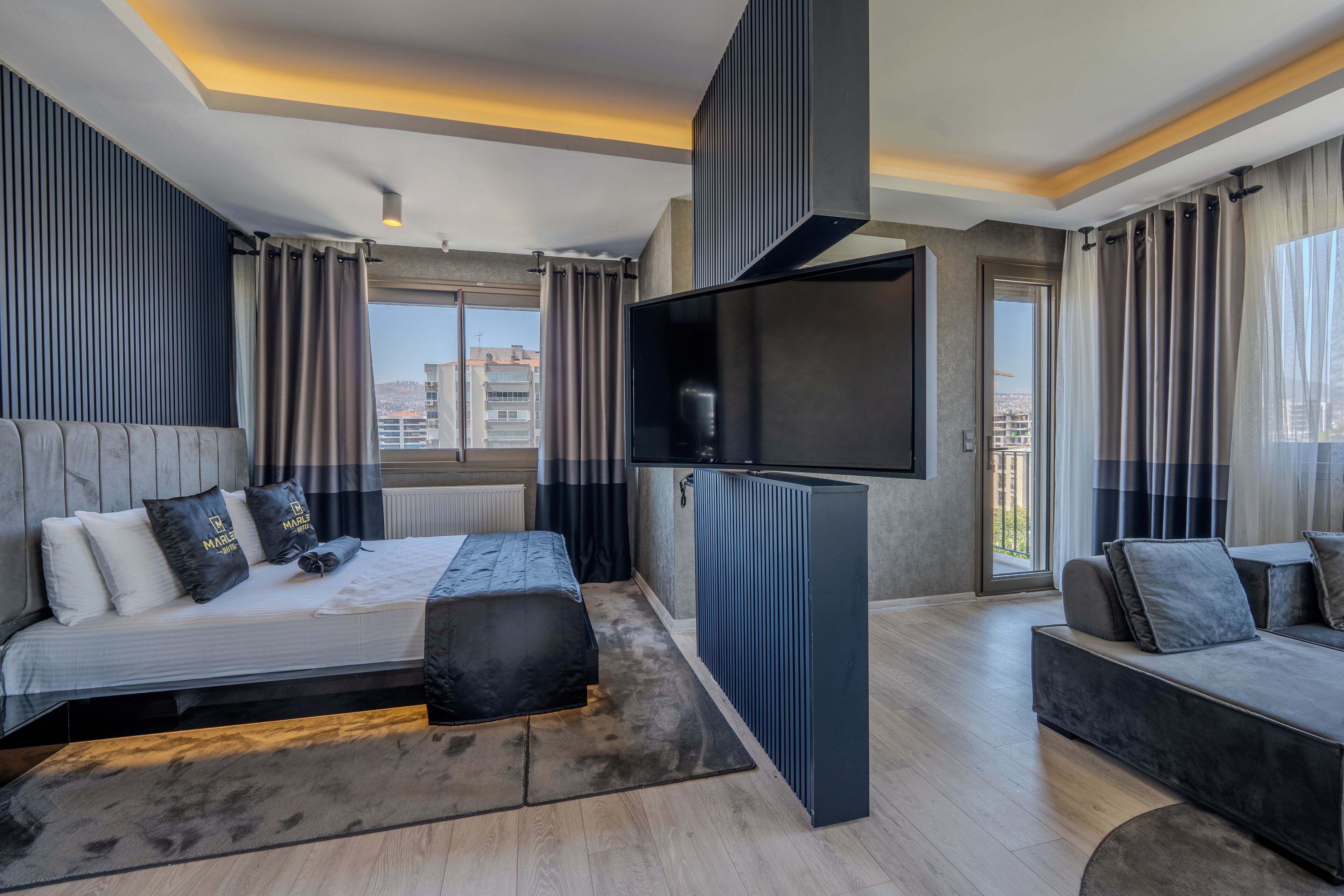 A modern bedroom with a bed, a sofa, a TV, and a view of the city.