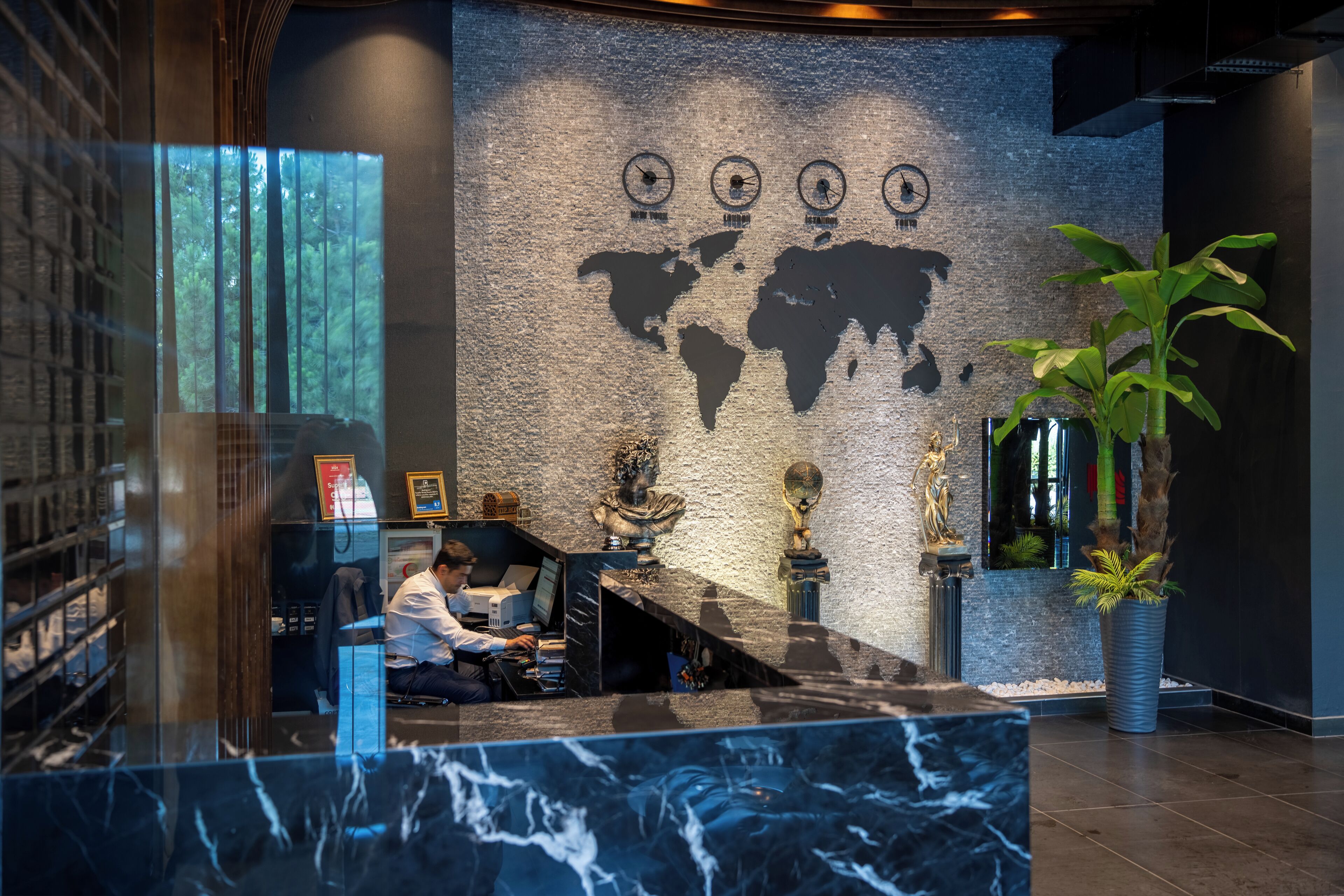 Una mesa de recepción con encimera de mármol, un mural de un mapa mundial y una estatua.