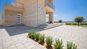 A modern two-story building with a flat roof, a balcony on the upper floor, and a paved courtyard with small plants. - Villa Morella with Heated Pool (Sukošan)