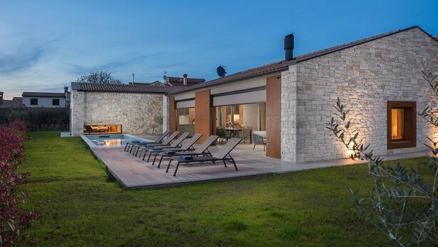 Een modern huis met een gevel van steen, een zwembad en buitenmeubilair.