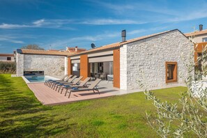 Une maison moderne avec une façade en pierre, une piscine et un patio équipé de chaises longues.