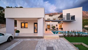 Una casa moderna de dos pisos con piscina, un porche cubierto y un coche en la entrada.