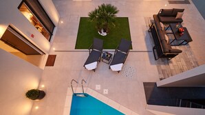 Un área de piscina en la azotea con dos sillones de descanso, una pequeña mesa con frutas y una palmera.