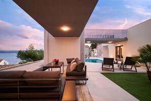 Uma área de estar moderna ao ar livre, com piscina, assentos e vista para o mar.