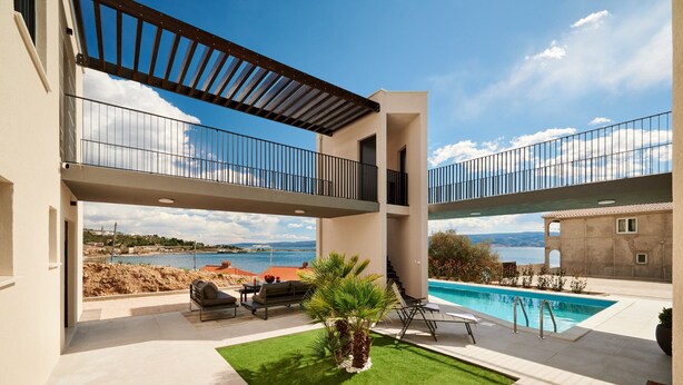 Una villa moderna con piscina, mobiliario de exterior y vistas al mar.