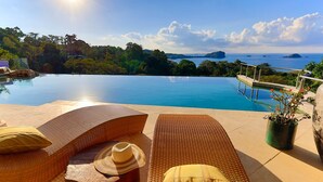A poolside area with lounge chairs, a sun umbrella, and a potted plant. - 10BR Luxury Ocean View Villa • Walk to Beaches • Huge Pool • Private Cinema (Manuel Antonio)