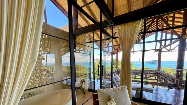 A room with a large glass window, a bathtub, and a wooden deck with a view of the ocean. - 10BR Luxury Ocean View Villa • Walk to Beaches • Huge Pool • Private Cinema (Manuel Antonio)