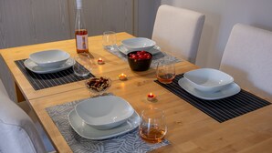 Ruokapöytä on katettu valkoisilla lautasilla, kulhoilla, laseilla ja siinä on myös viinipullo.