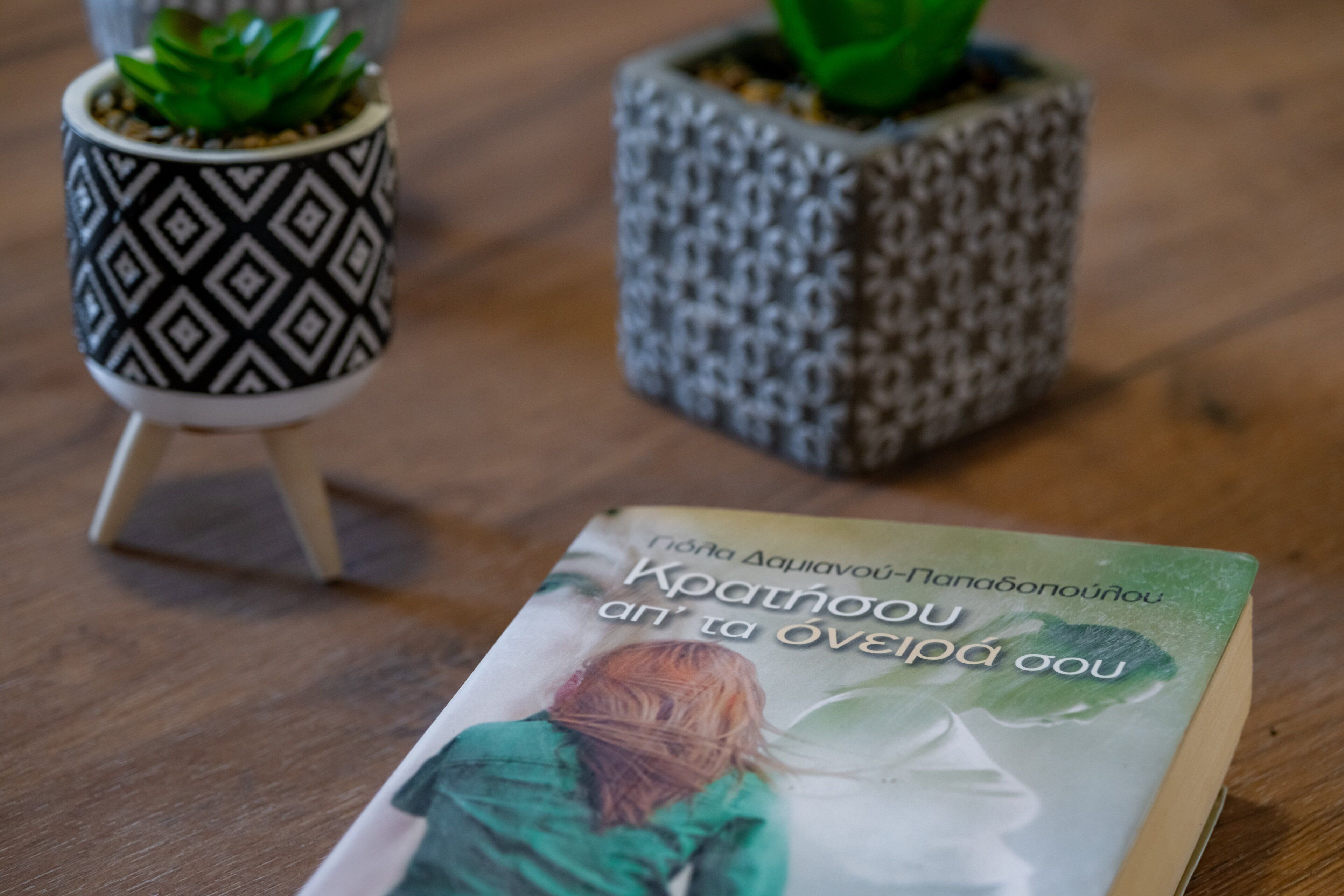 A book titled 'Kratnaou' on a wooden surface with two patterned potted plants.